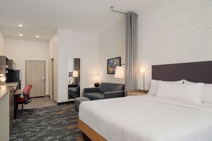 A hotel room with a bed, a desk, a chair, a sofa, and a painting on the wall. - Home2 Suites By Hilton Lafayette I-10 (Lafayette)