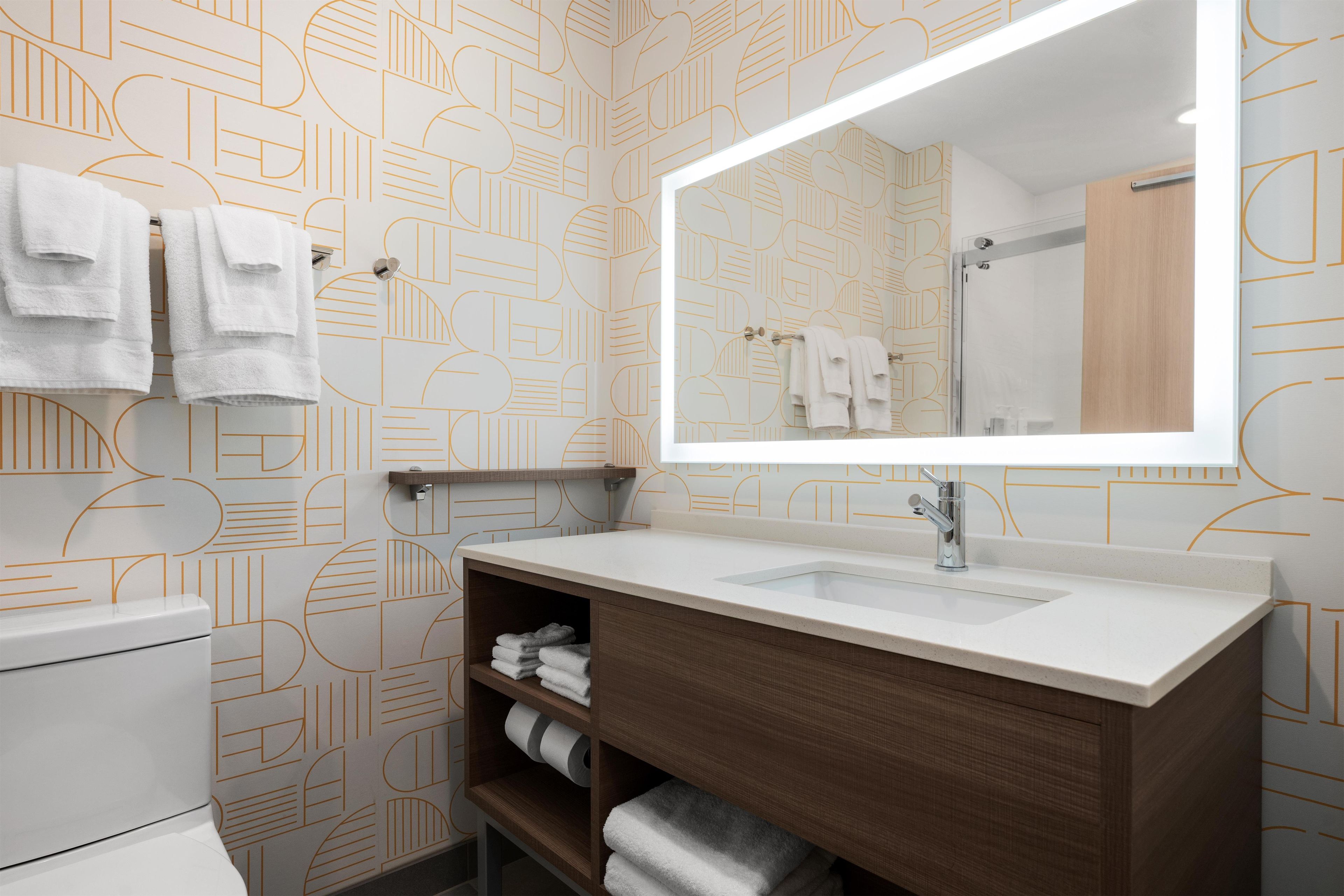 A bathroom with a geometric patterned wall, a white sink with a mirror, and towels on the wall and shelves.
