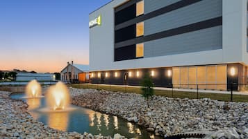 A modern building with a sign reading 'HOME 2' and a water feature with fountains.
