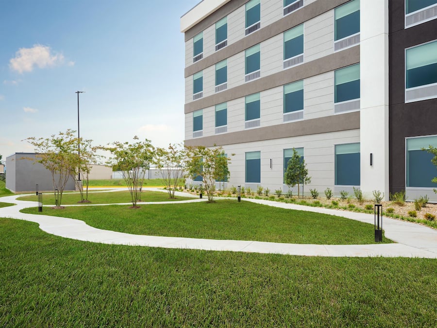 A modern building with a flat roof, multiple windows, and a landscaped area with a pathway.