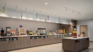 A modern hotel reception area with a counter, coffee machines, and a fruit display. - Home2 Suites By Hilton Lafayette I-10 (Lafayette)