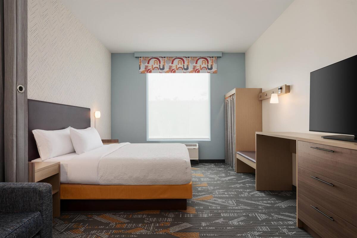 A hotel room with a bed, a desk, a chair, a television, and a window with a view.