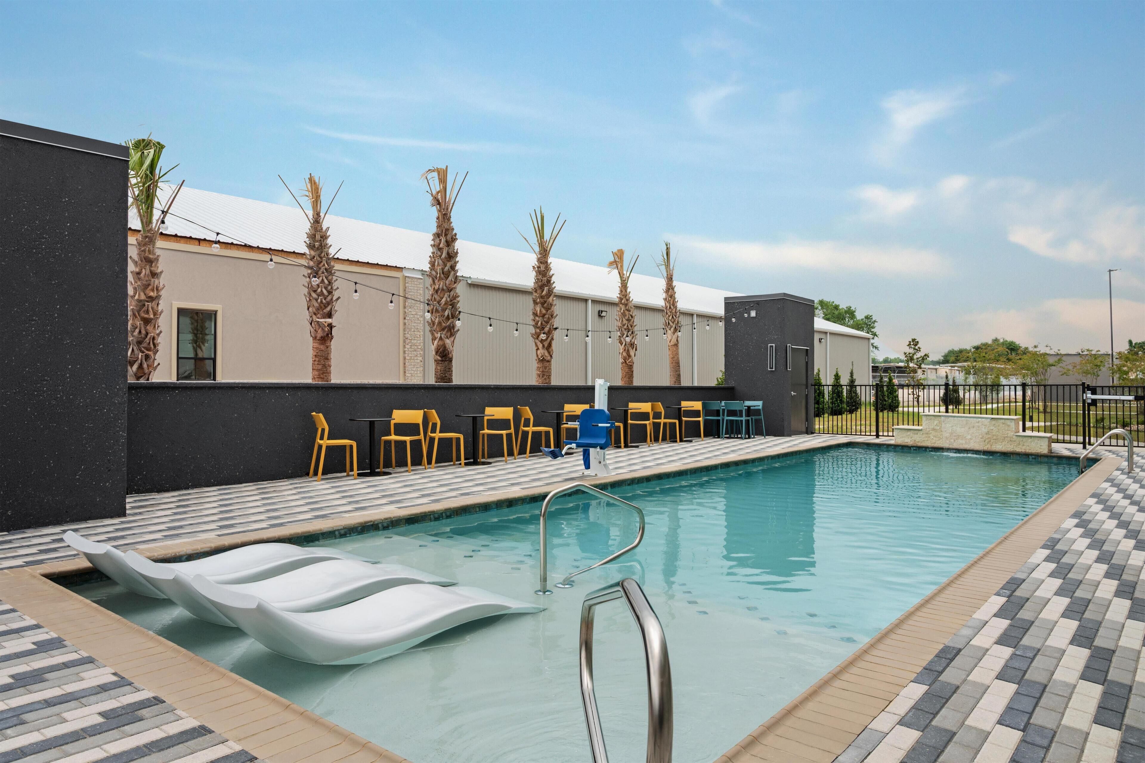 A swimming pool with lounge chairs, a small building, and palm trees.