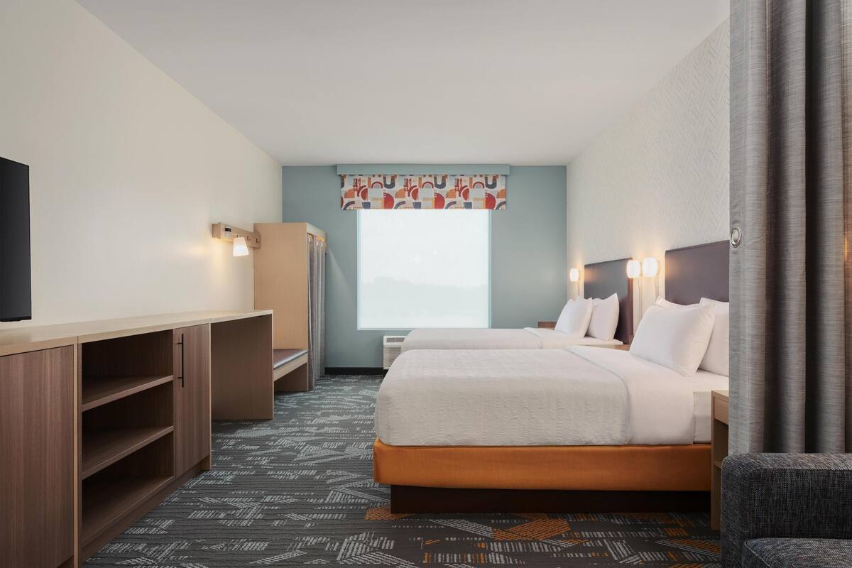 A hotel room with a bed, a desk, a chair, a television, and a window with a view.
