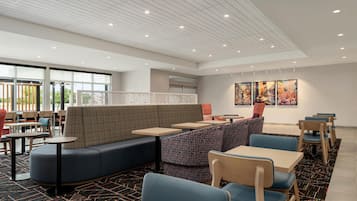 A modern indoor seating area with sofas, tables, and chairs, large windows, and artwork on the walls.
