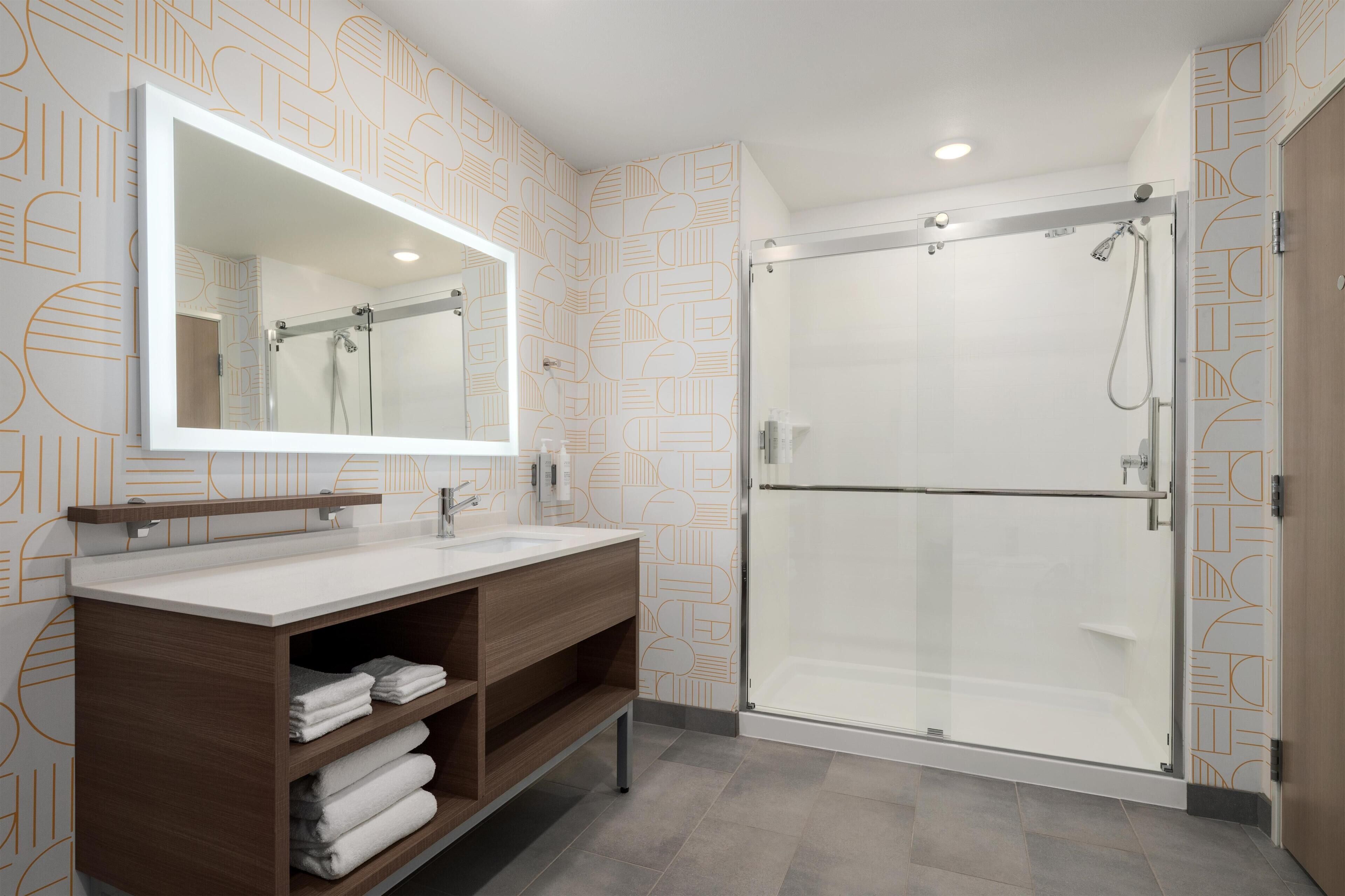 A modern bathroom with a glass-enclosed shower, a large mirror, and a wooden vanity.