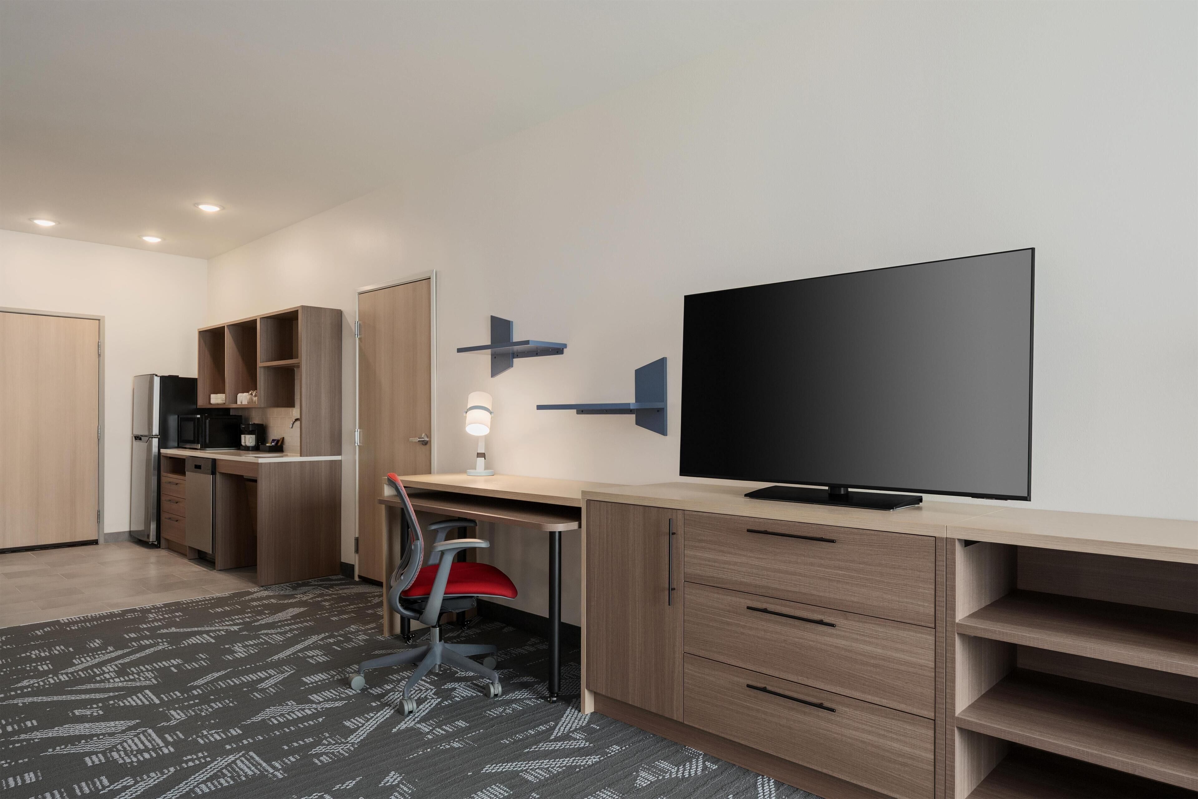 A modern room with a desk, chair, television, and kitchen area.