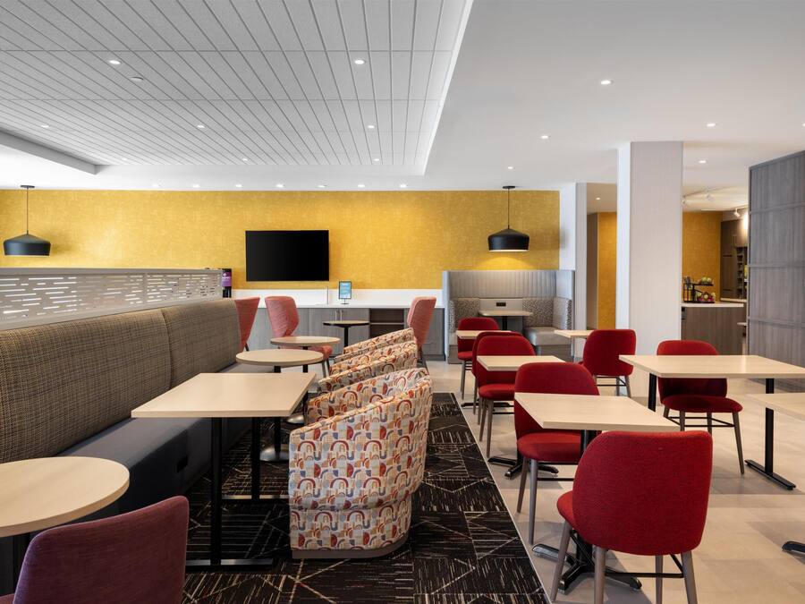 A modern restaurant with a high ceiling, a flat-screen TV, and a variety of seating options including booths and tables.