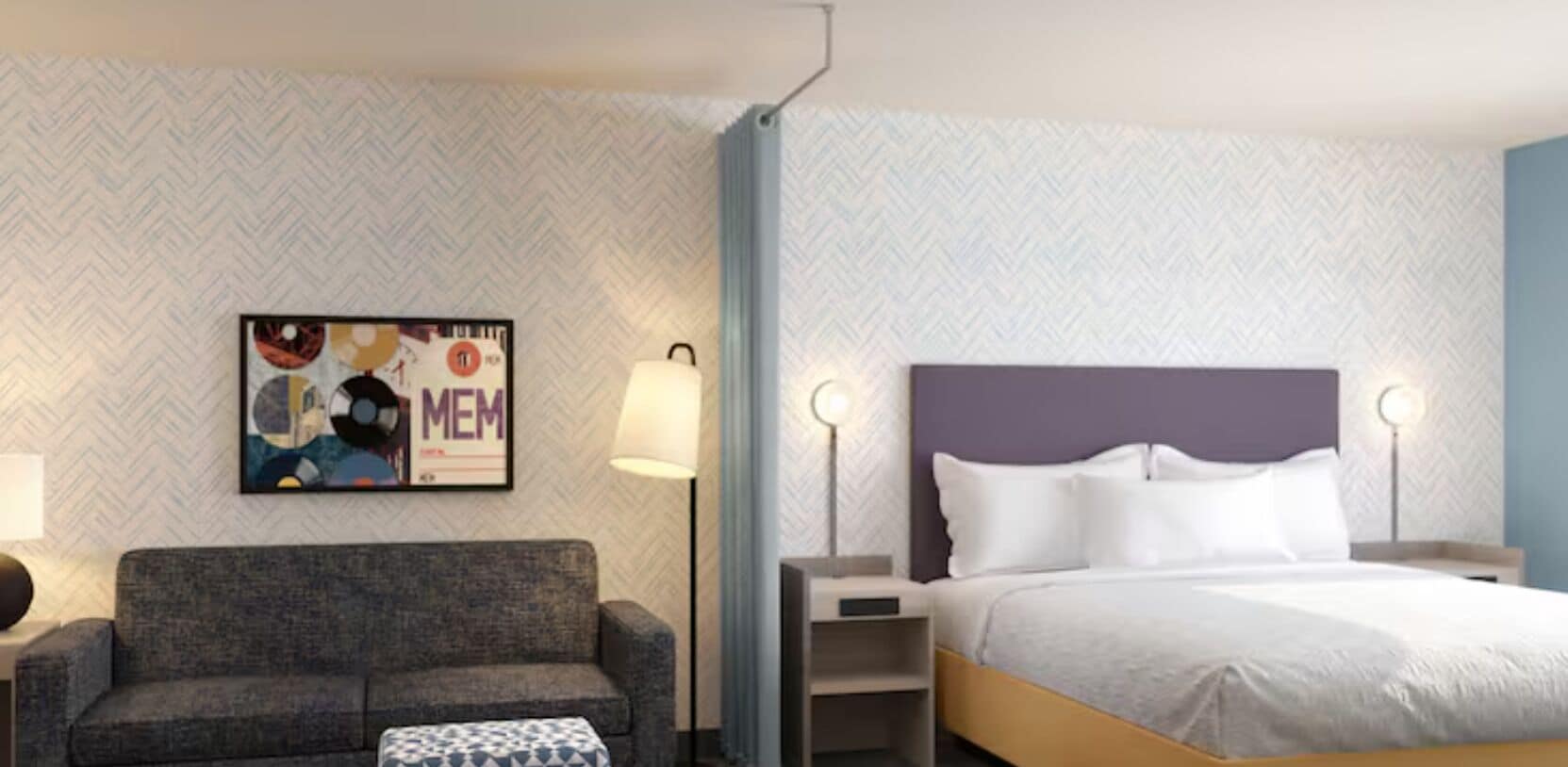 Hotellihuone, jossa on sänky, sohva, yöpöytä, lamppu ja kuviollinen tapetti seinällä.