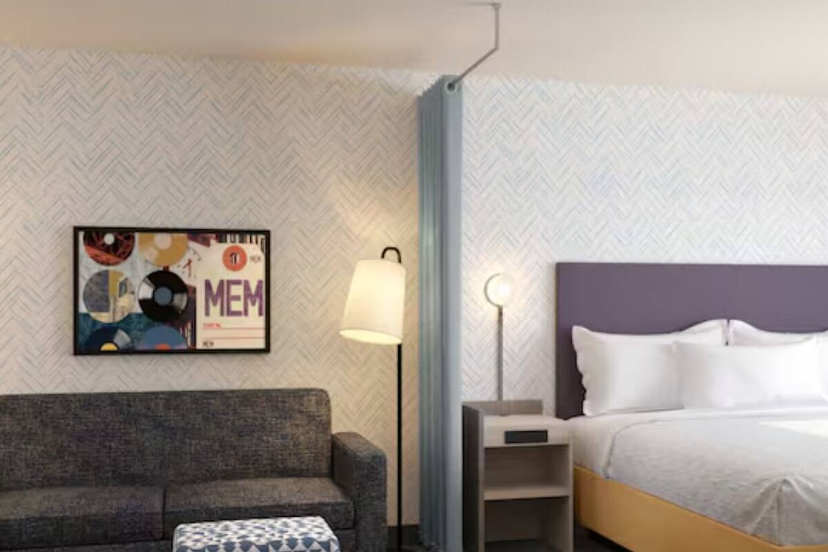 Habitación de hotel con cama, sofá, mesita de noche, lámpara y un papel tapiz estampado.