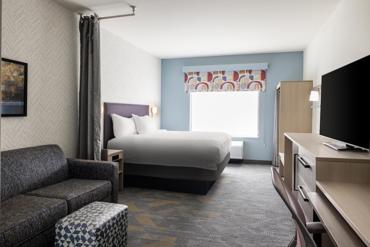 Una habitación de hotel con cama, sofá, televisión y escritorio.