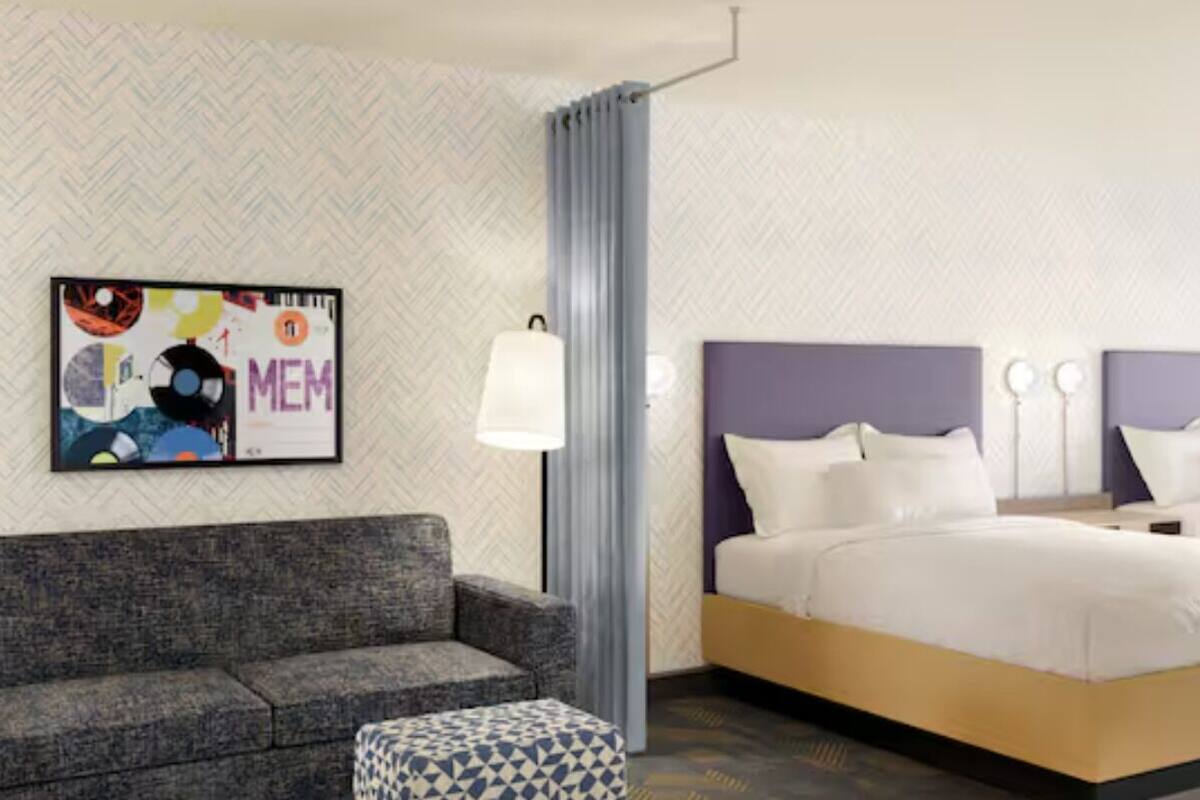 Habitación de hotel con sofá, cama, mesita de noche, lámpara y papel tapiz estampado.