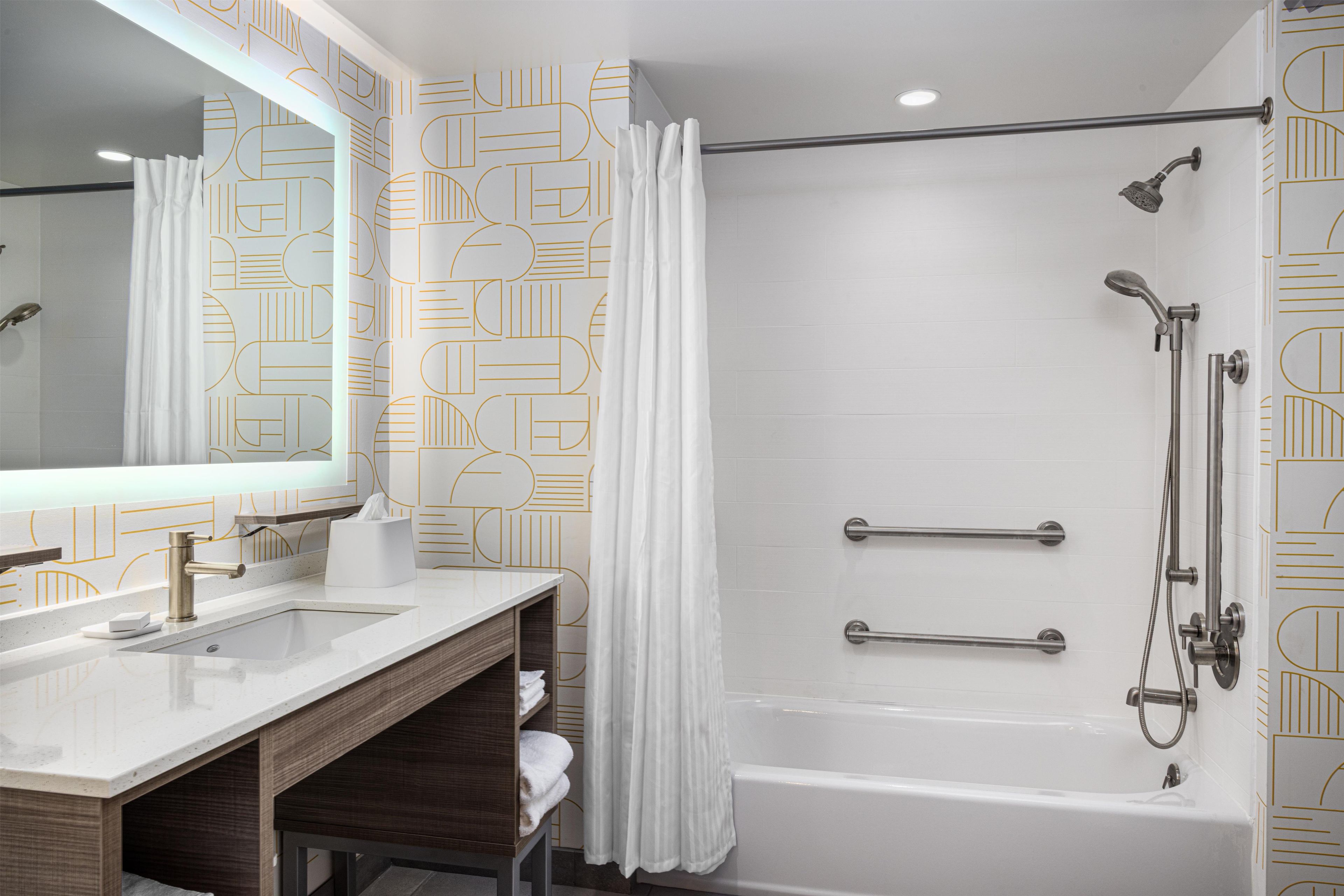 A modern bathroom with a large mirror, two sinks, a shower with a handheld showerhead, and a bathtub.