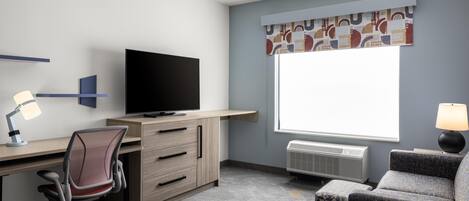 Habitación de hotel con escritorio, silla, televisor, ventana con cortinas y un sofá.