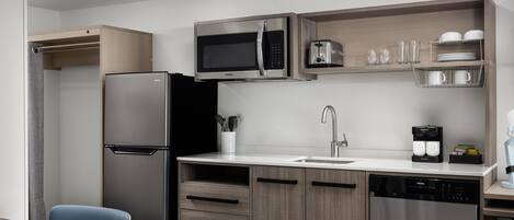 A compact kitchen with a refrigerator, microwave, coffee maker, and dishwasher.