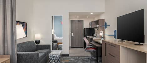 Une chambre d’hôtel comprenant un lit, un canapé, un bureau, une télévision et une kitchenette.