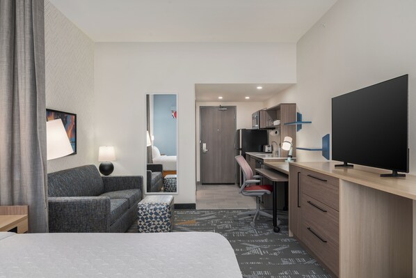 Una habitación de hotel con cama, sofá, escritorio, televisor y kitchenette.
