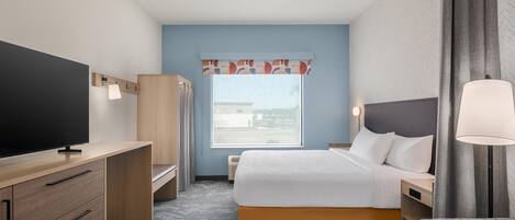 Habitación de hotel con cama, mesita de noche, lámpara, televisor, armario y ventana con vistas.