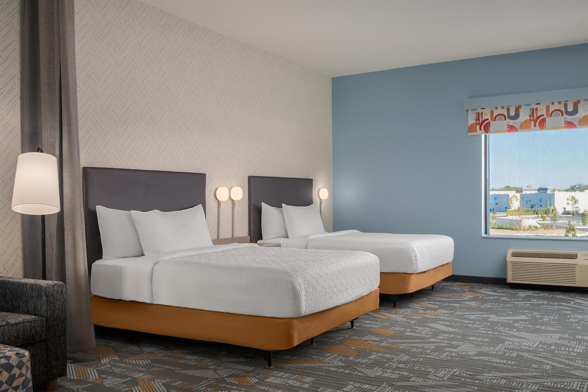 A hotel room with two beds, a sofa, a lamp, and a large window with a view.