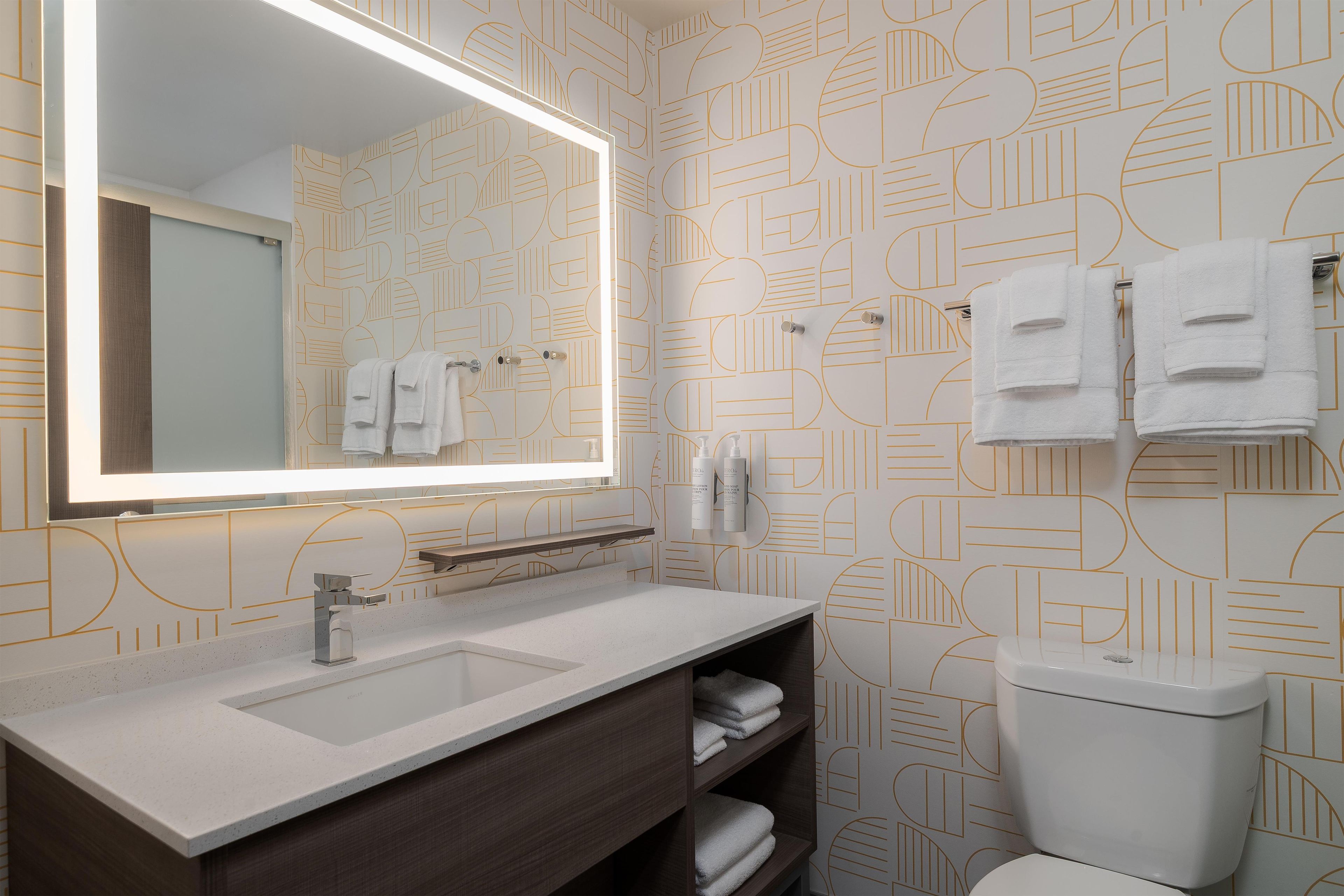 A bathroom with a large mirror, two sinks, a toilet, and towels hanging on the wall.