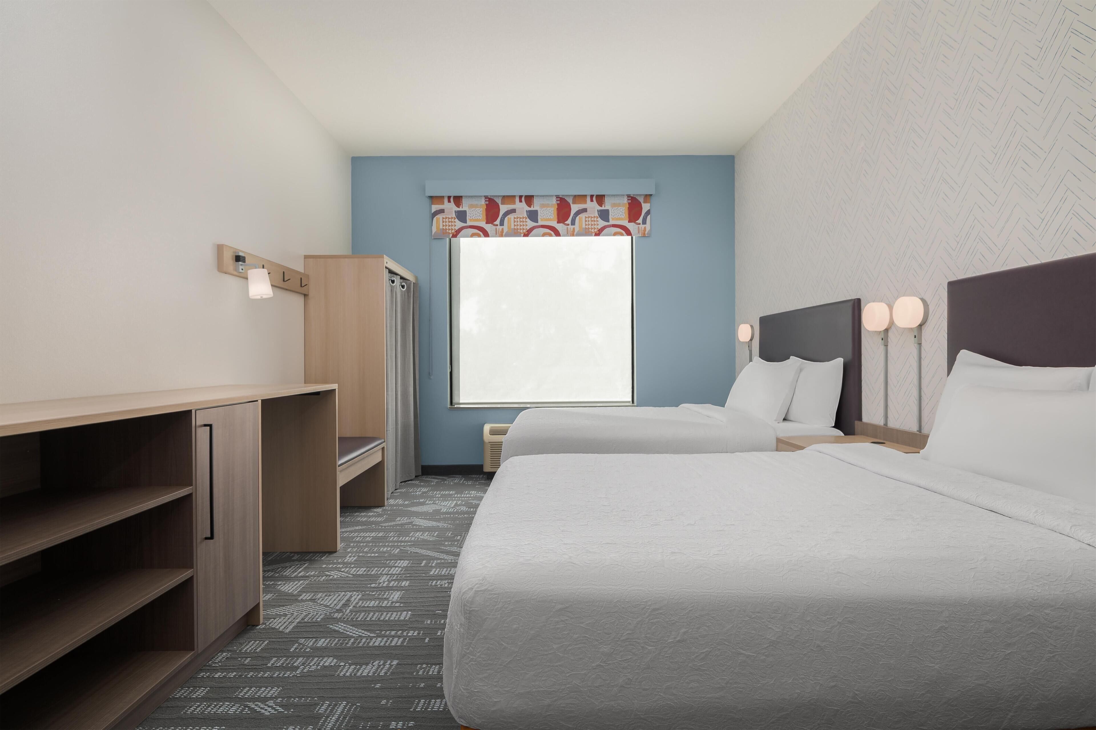A hotel room with a bed, bedside tables, a wardrobe, a window with a curtain, and a patterned carpet.