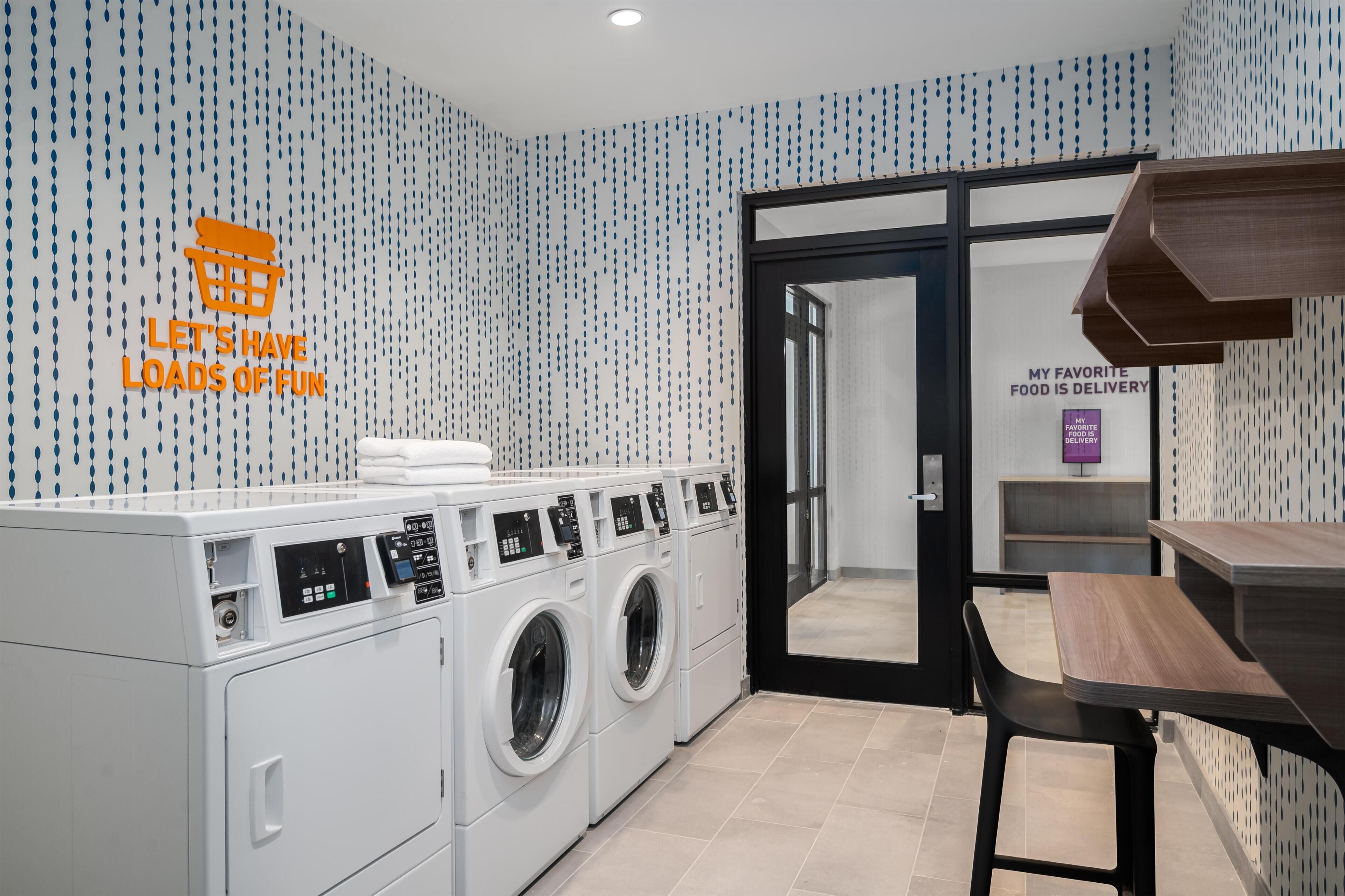 Un espace buanderie moderne comprenant un lave-linge fixé au mur, un étendoir et une table avec des chaises.
