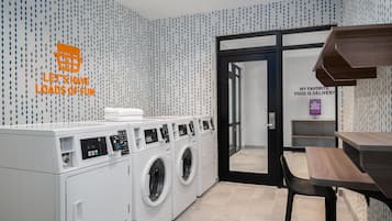 Un espace buanderie moderne comprenant un lave-linge fixé au mur, un étendoir et une table avec des chaises.