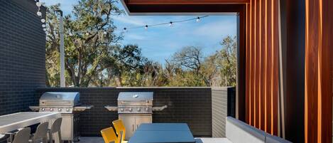 Een terras buiten met een barbecue, tafels en stoelen.
