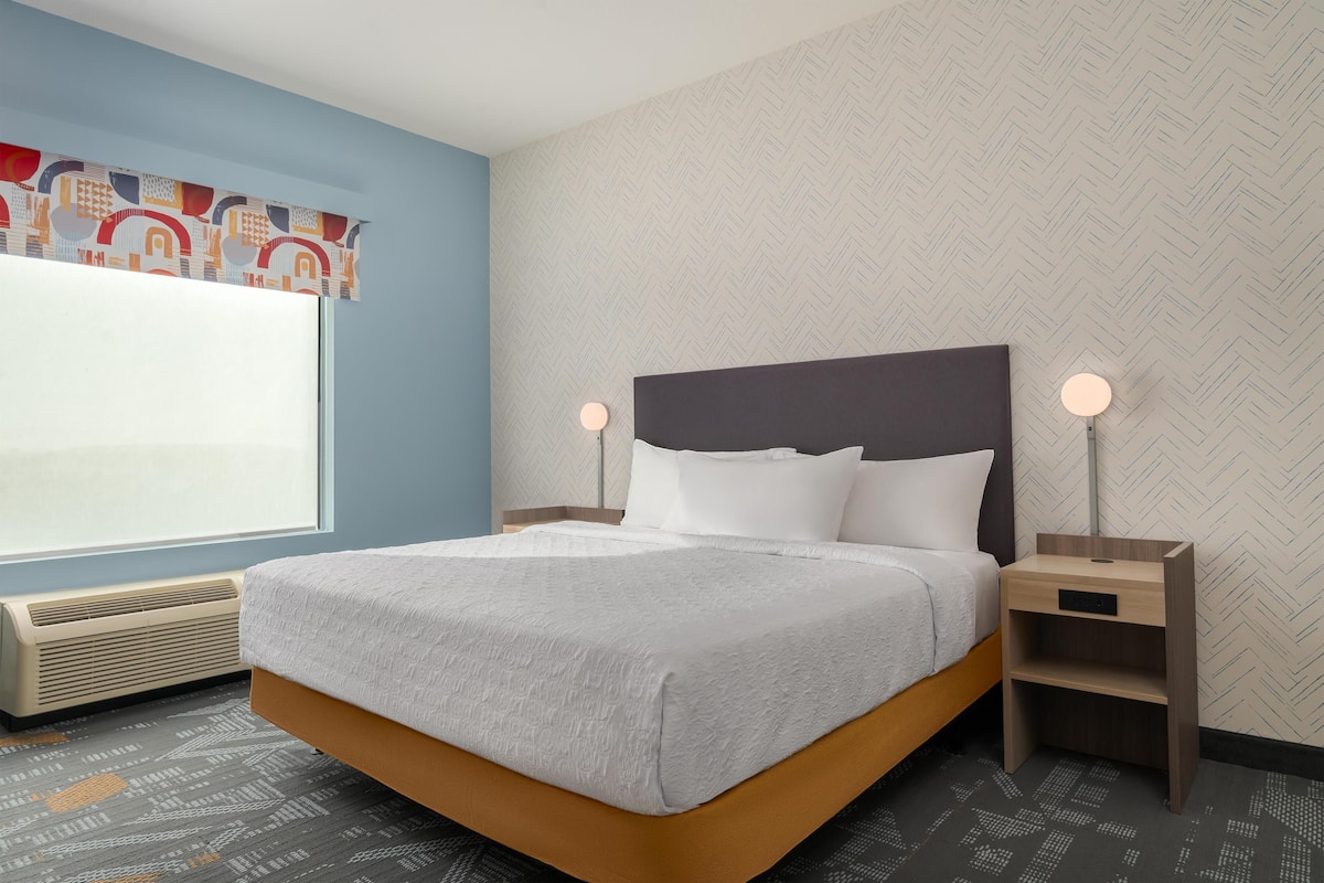 A modern hotel room with a bed, bedside tables, a window, and a patterned wall.