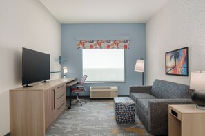 Una habitación de hotel moderna con televisión de pantalla plana, un sofá, un escritorio y una ventana con cortina estampada.