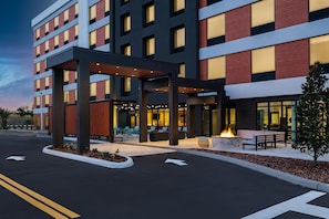 Ein modernes Hotel mit überdachter Außenbereich-Sitzgelegenheit, einem Feuerbereich und wolkenlosem Himmel.