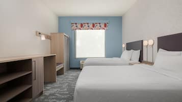 Une chambre d’hôtel avec deux lits, un bureau, une armoire et une fenêtre avec des rideaux à motifs.