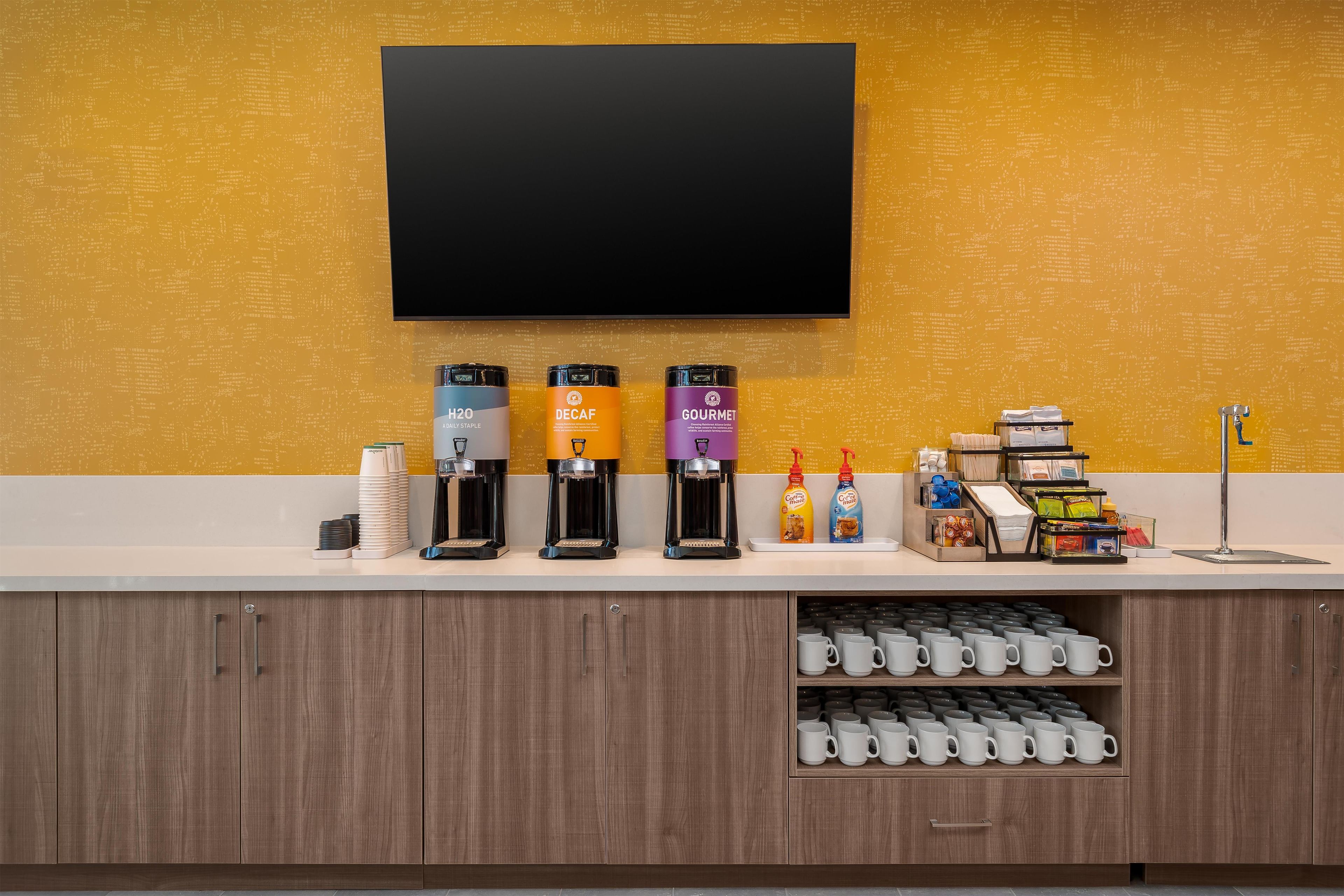 Un espace dédié au café, équipé de plusieurs machines à café, d’un téléviseur à écran plat et d’un comptoir où sont exposés divers articles.
