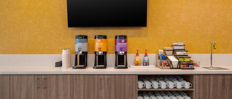 A coffee station with multiple coffee makers, a flat-screen TV, and a counter with various items.