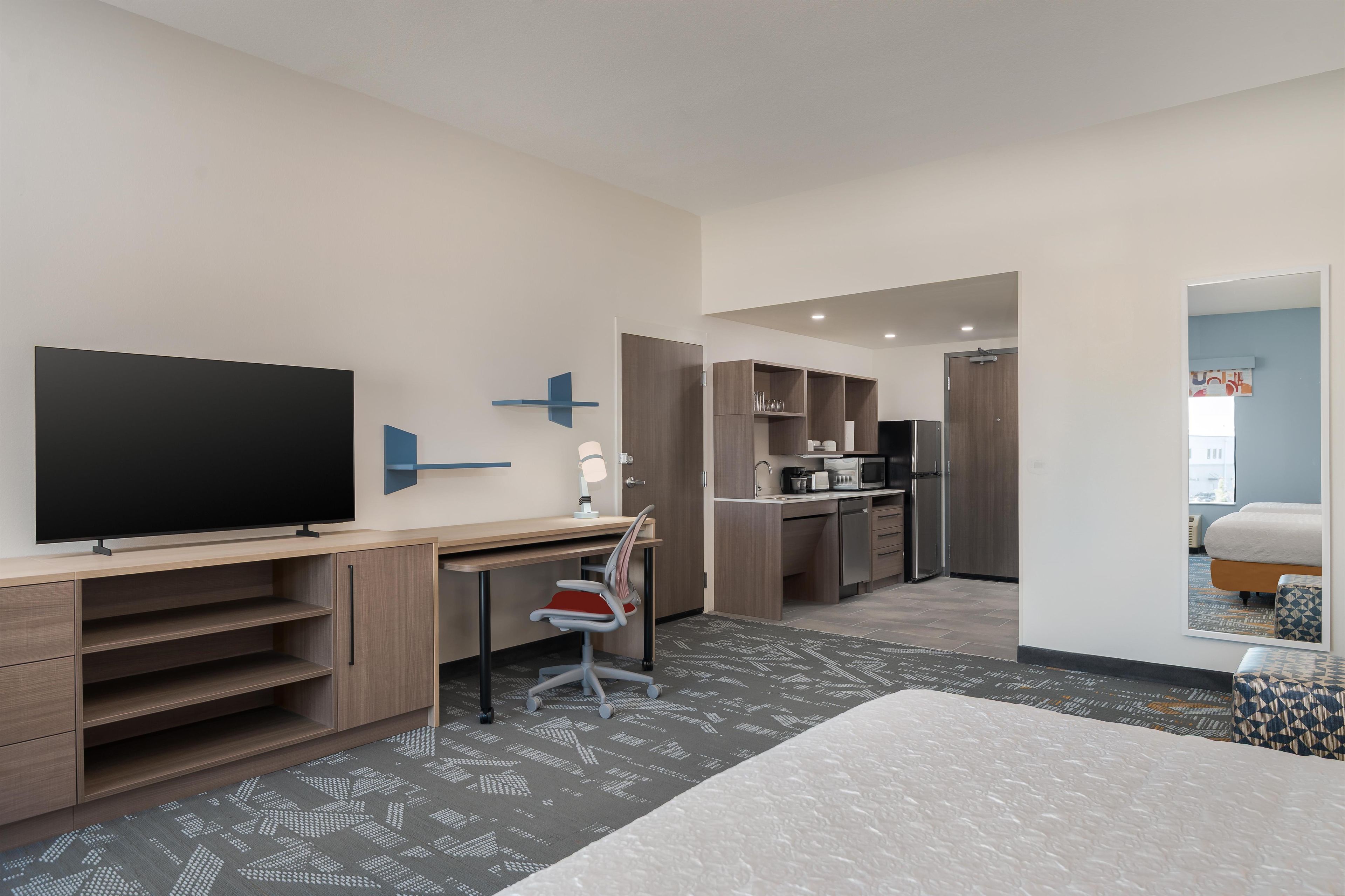Una habitación de hotel moderna con una televisión de pantalla plana grande, un escritorio con una silla, una kitchenette y una cama.
