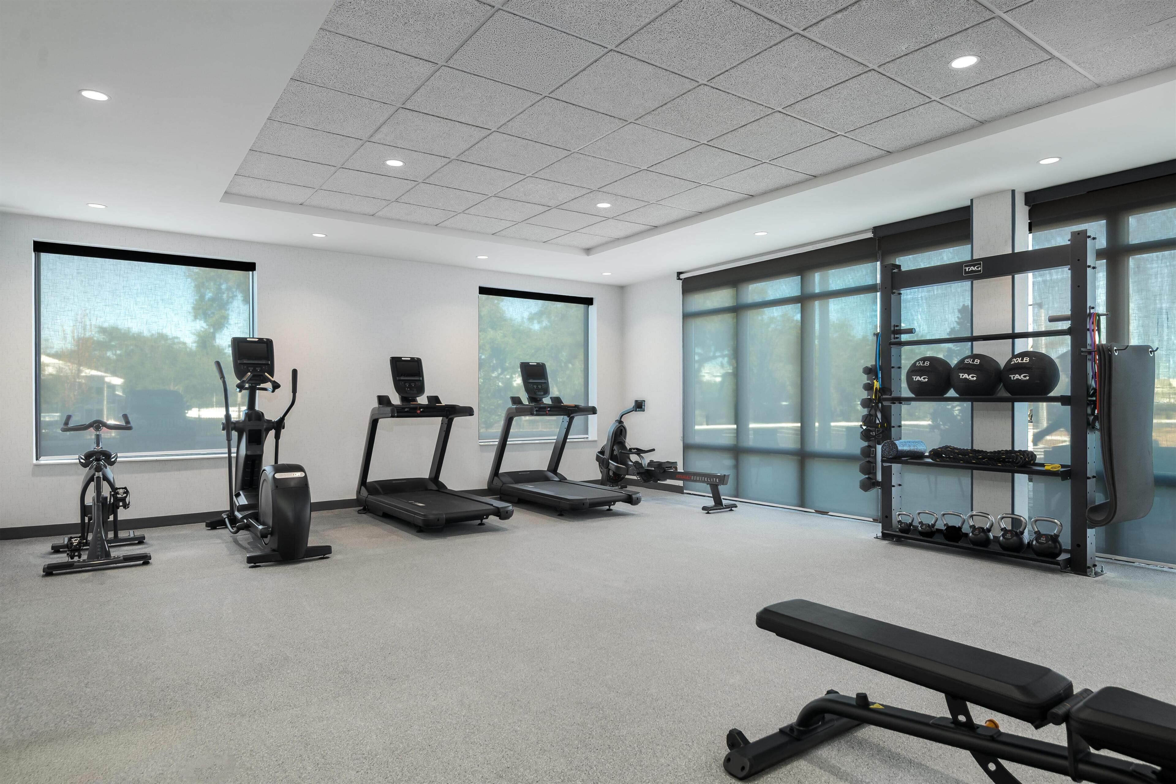 Un gimnasio con cintas de correr, elíptica, banco y una barra de pesas.