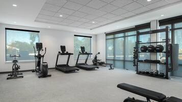 Un gimnasio con cintas de correr, elíptica, banco y una barra de pesas.