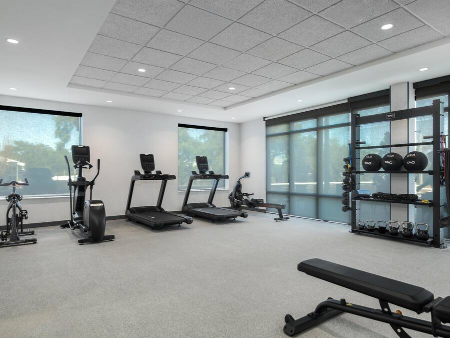 Un gimnasio con cintas de correr, elíptica, banco y una barra de pesas.