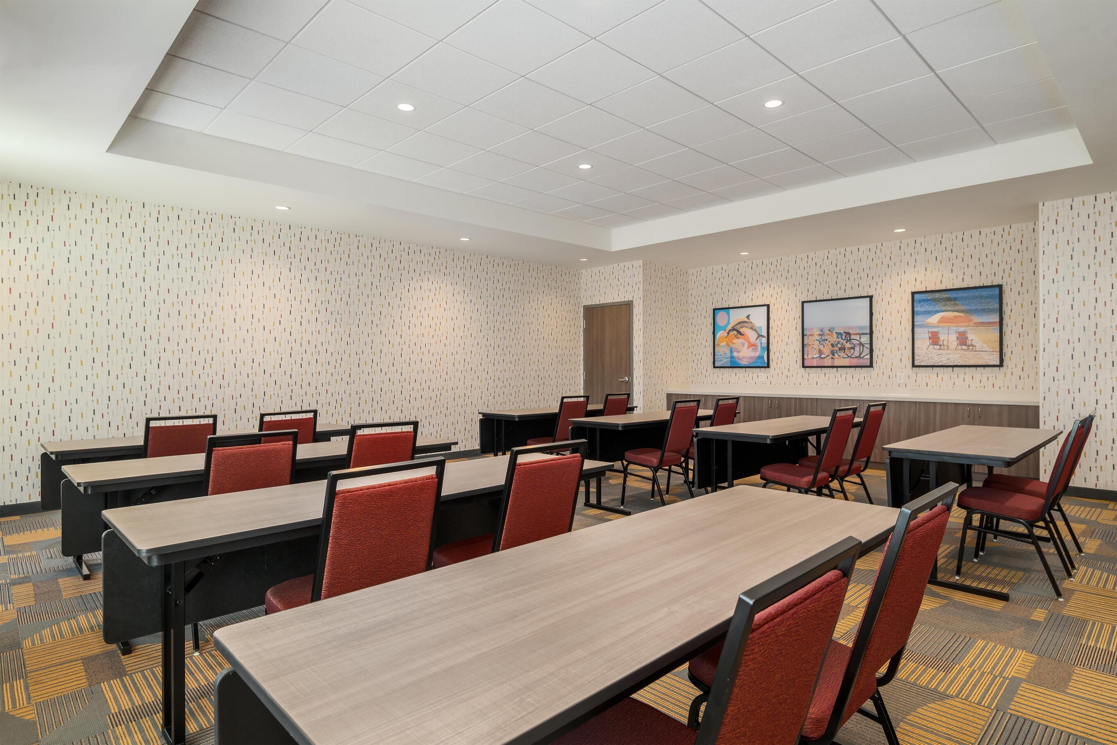 A conference room with multiple tables and chairs, patterned wallpaper, and framed artwork on the walls.