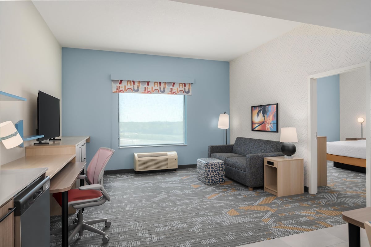 A hotel room with a desk, chair, sofa, bedside table, lamp, and a bed.
