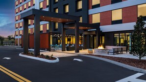 Ein modernes Hotel mit überdachter Außenbereich-Sitzgelegenheit, einem Feuerbereich und wolkenlosem Himmel.