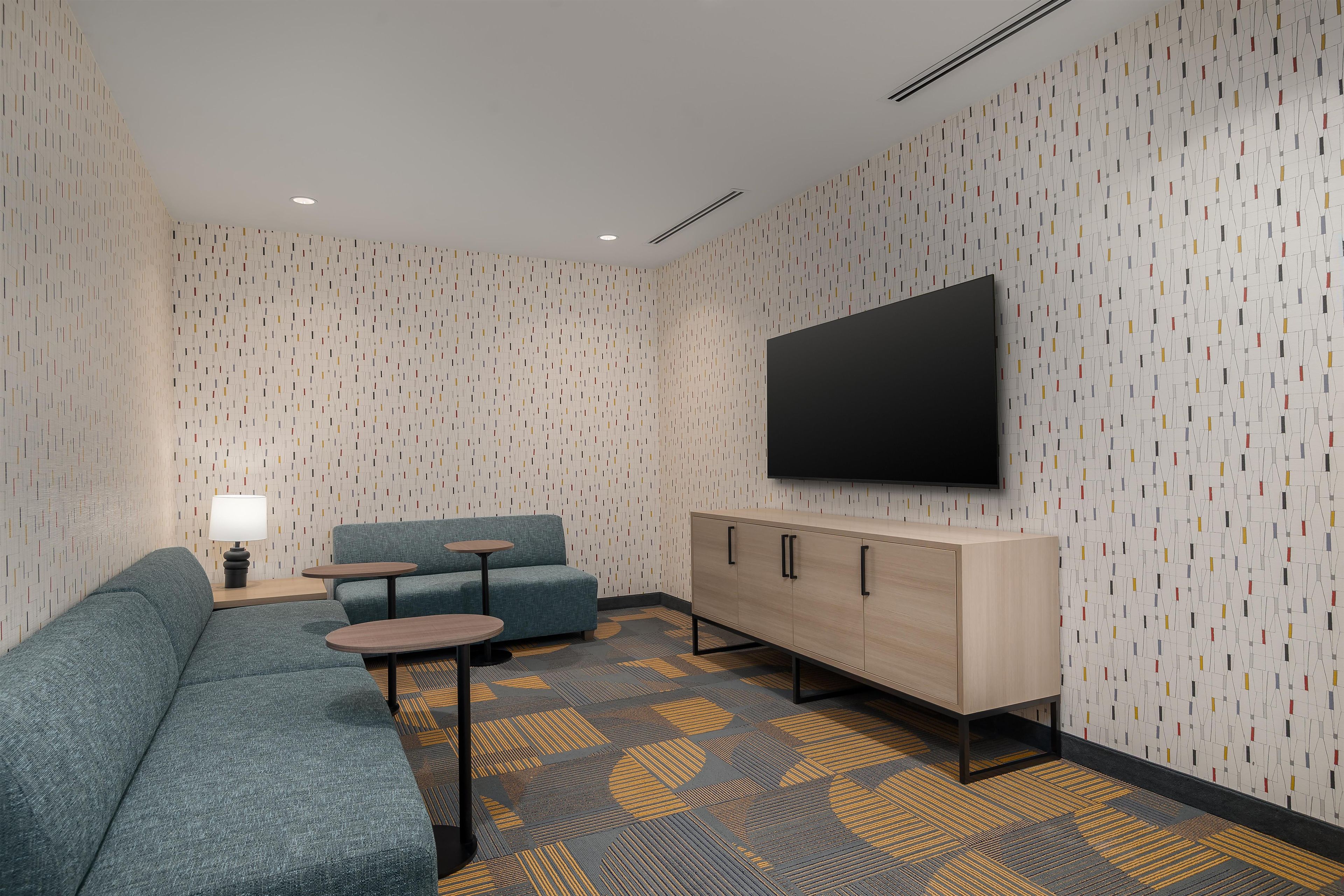 Una habitación de hotel moderna con un sofá modular, una mesita, un armario y un televisor de pantalla plana montado en la pared.