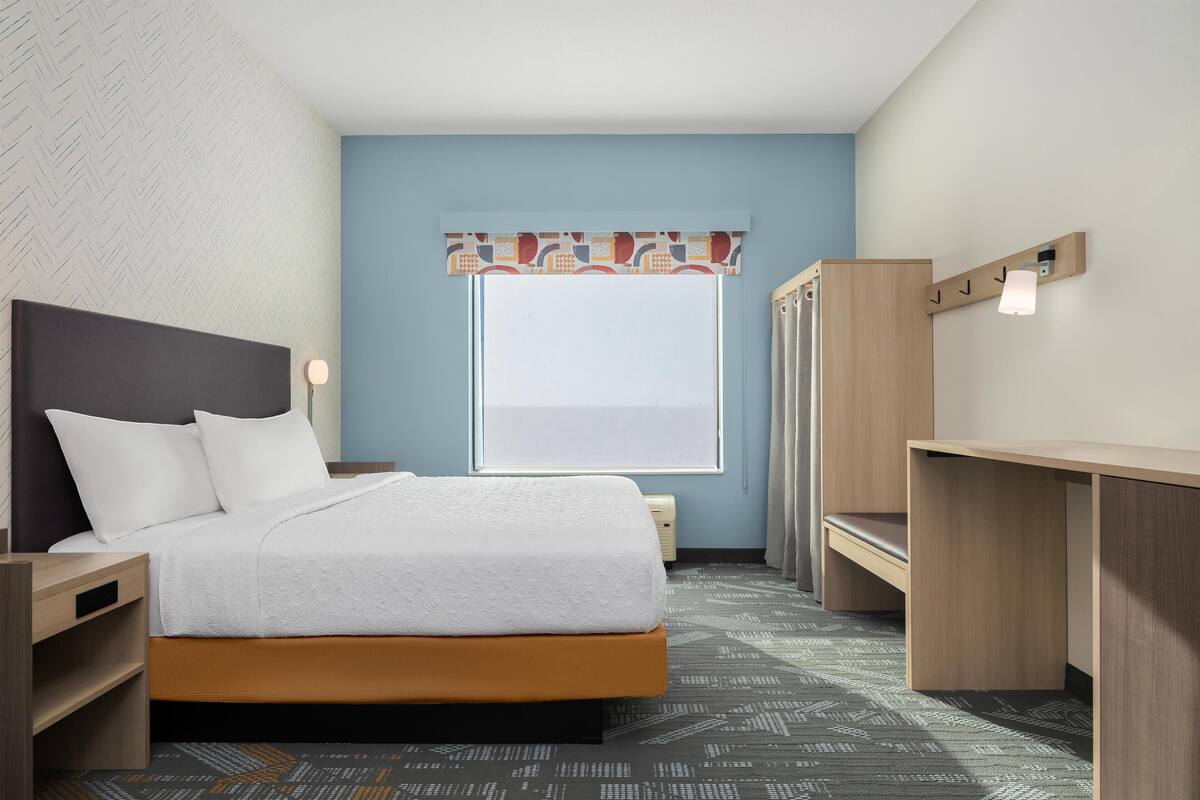 A hotel room with a bed, bedside tables, a desk, a wardrobe, and a window with a view.
