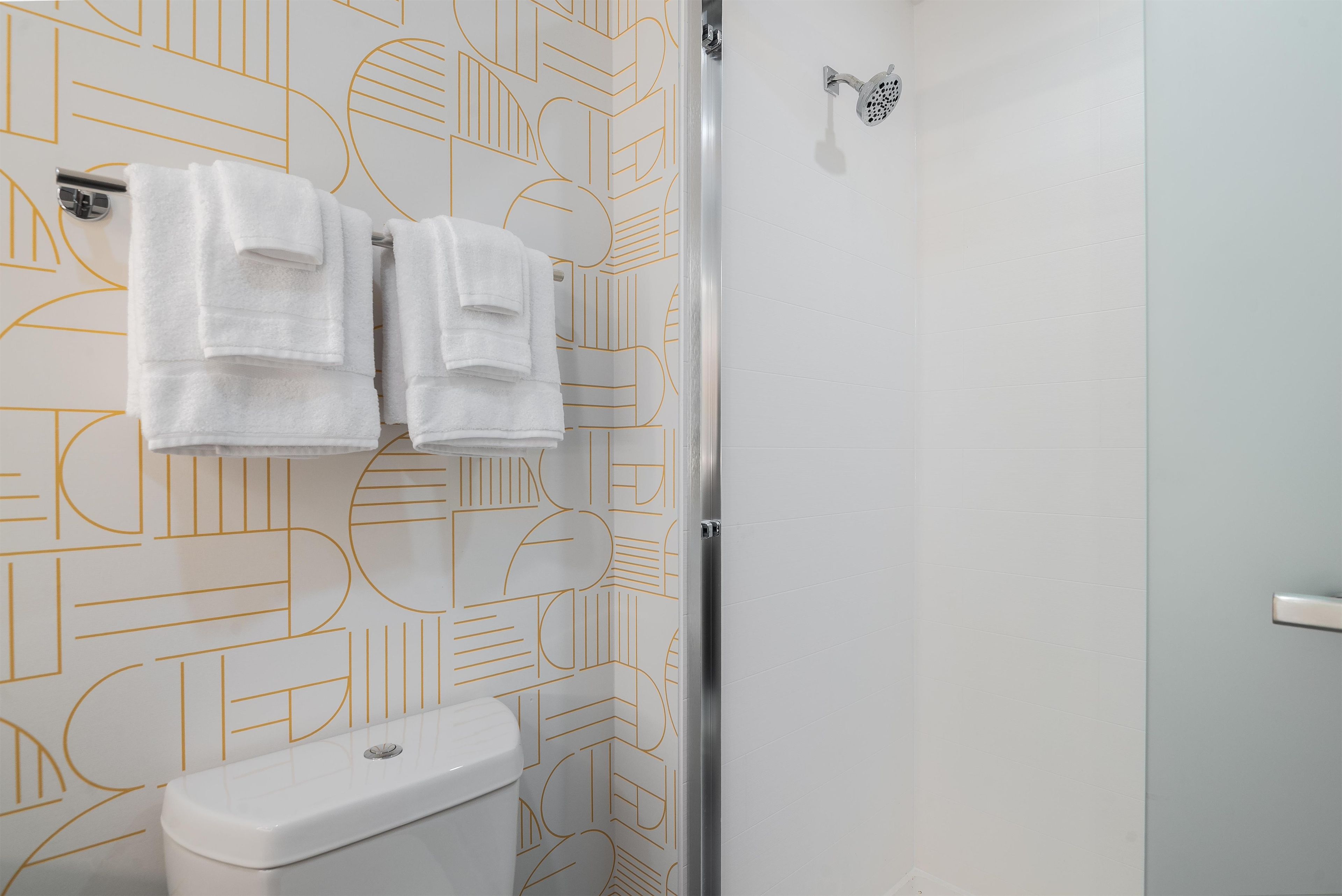 A bathroom with a toilet, a shower, and towels hanging on a rack.
