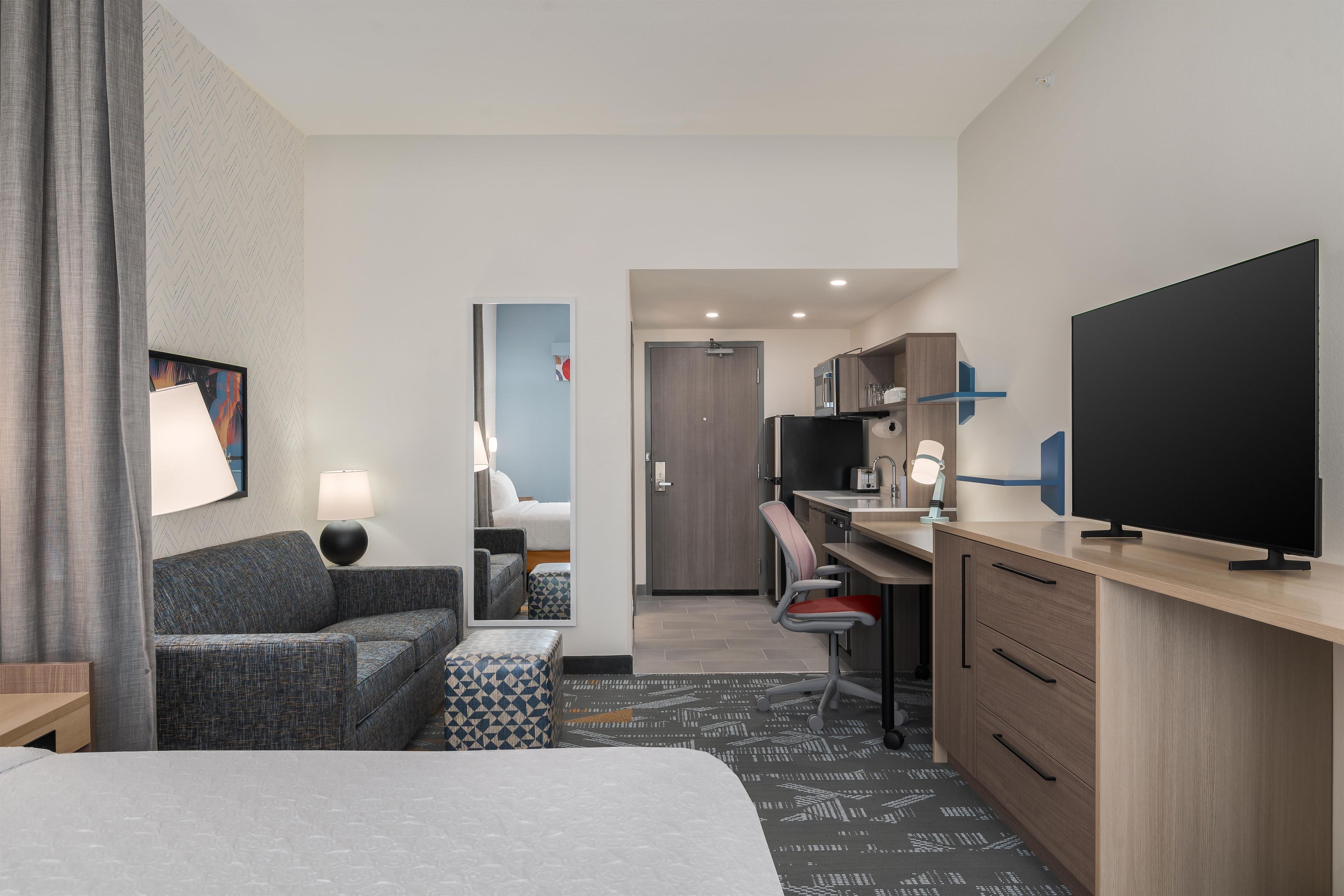 Ein Hotelzimmer mit Bett, Sofa, Schreibtisch mit Stuhl, Fernseher und einer Küchenzeile.