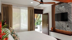 A modern hotel room with a large bed, a ceiling fan, a flat-screen TV mounted on a marble wall, and a view of the outdoors. - Hotel Sanctuarium Adults Only (La Fortuna)