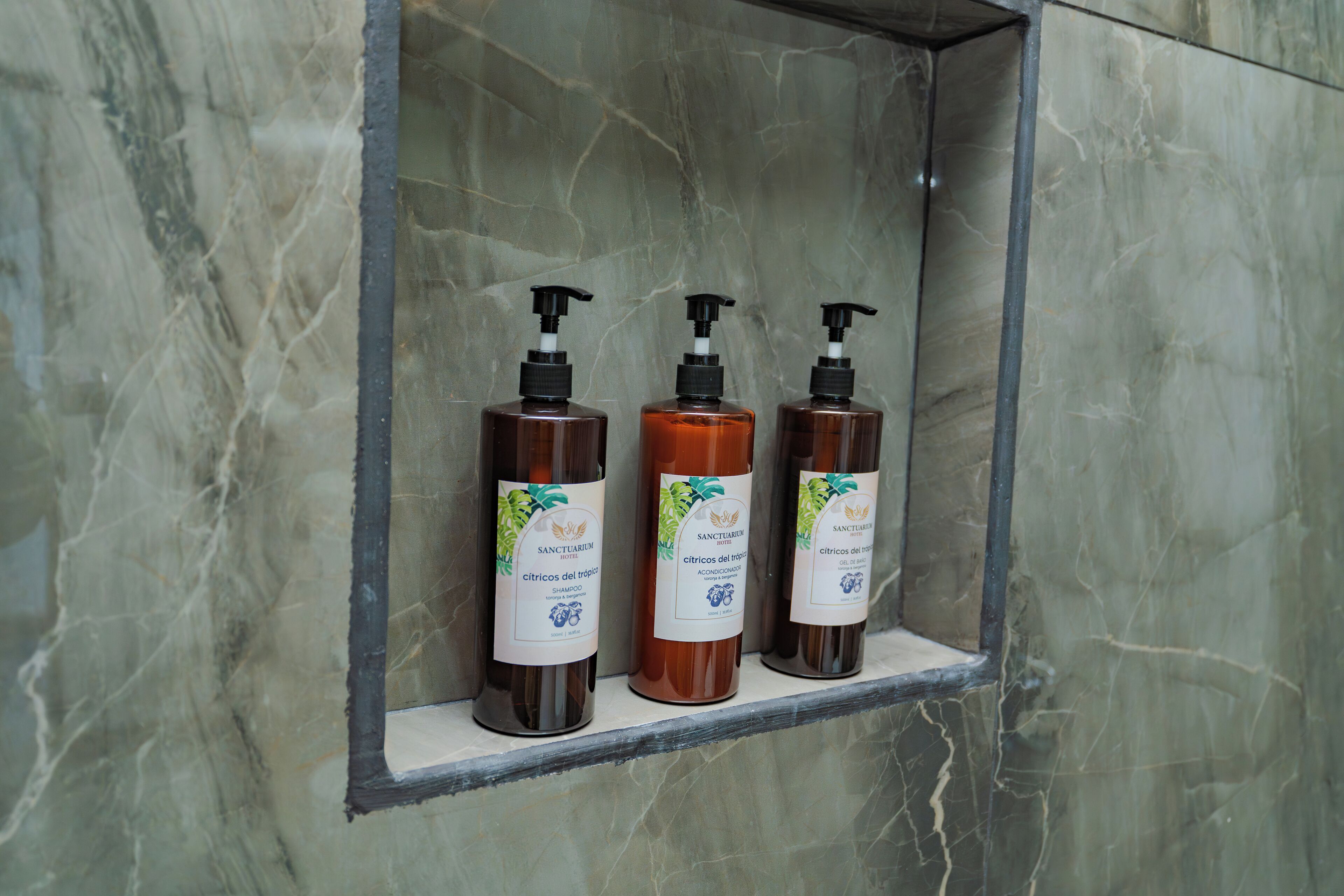 Three bottles of Sanctuary citrus shampoo in a marble display case.