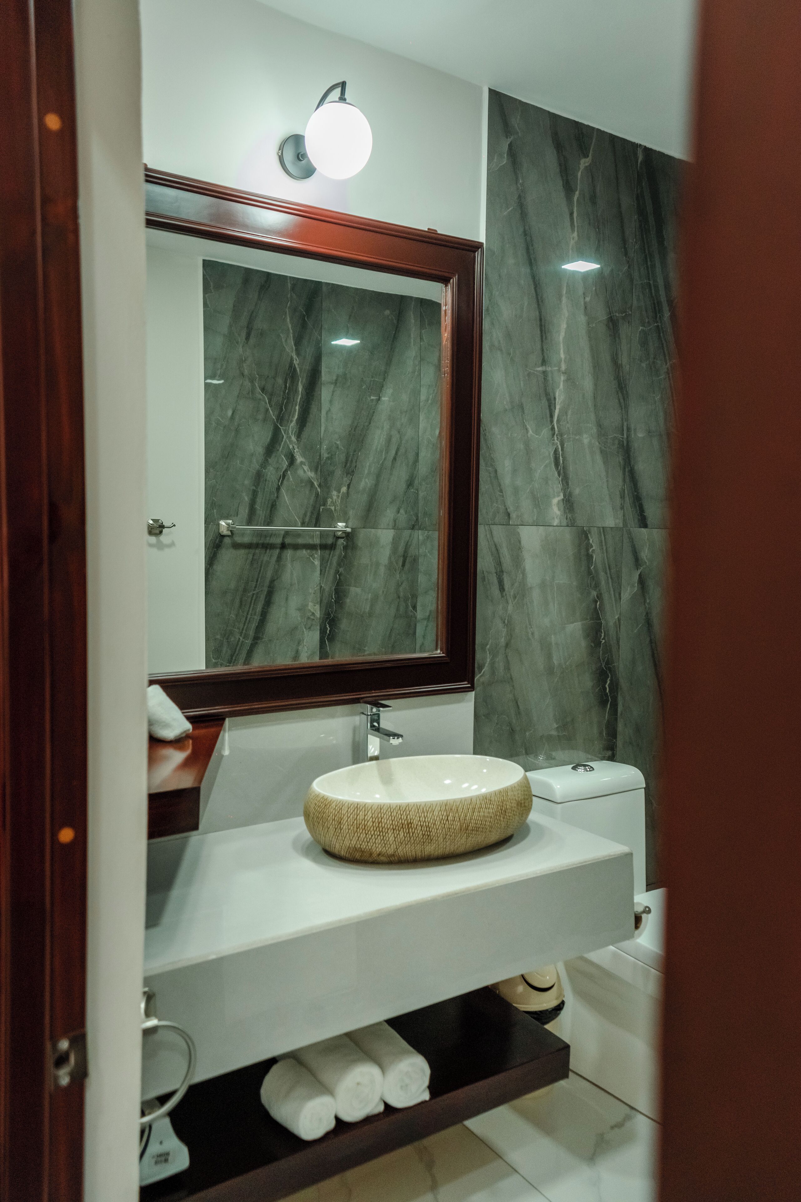 Un baño con pared de mármol, un lavabo redondo, un espejo y un perchero para toallas.