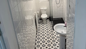 Ein kleines, schmales Badezimmer mit Toilette, Waschbecken und Duschbereich.