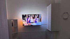 Ein Zimmer mit einem wandmontierten Flachbildfernseher, einem weißen Schrank, einem kleinen weißen Tisch und einem Heizkörper unter dem Fernseher.